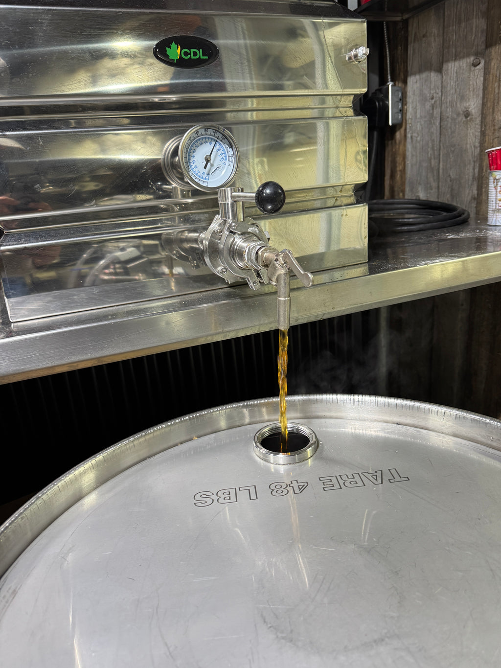Aluminum maple syrup container being filled with maple syrup from a tap system.